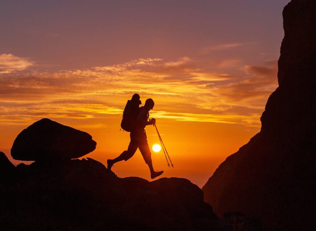 Person hiking on a mountain crest with a sunset in the background